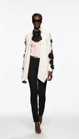 Model wearing a stylish outfit with a white jacket, pink shirt, and black pants on a white background